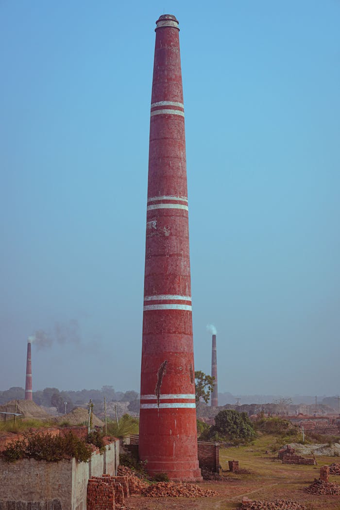 Red brick kiln chimney in rural landscape, clear sky backdrop.