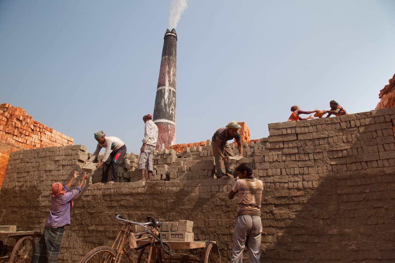 Laborers building a brick structure near a smokestack in Gabtoli, Dhaka, Bangladesh.